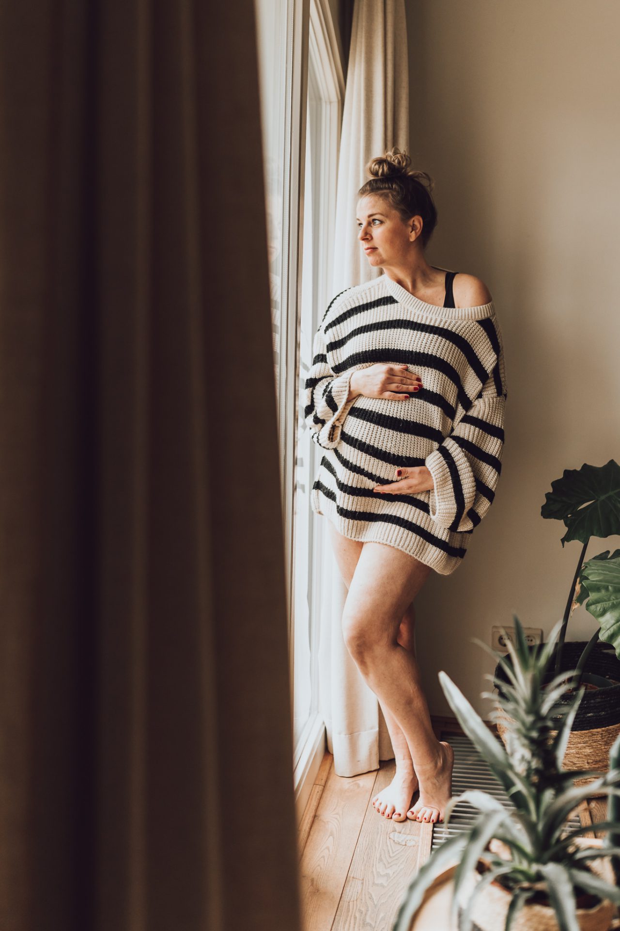 Zwangerschapsfotoshoot door flow photography, zwangere kijkend naar buiten via raam